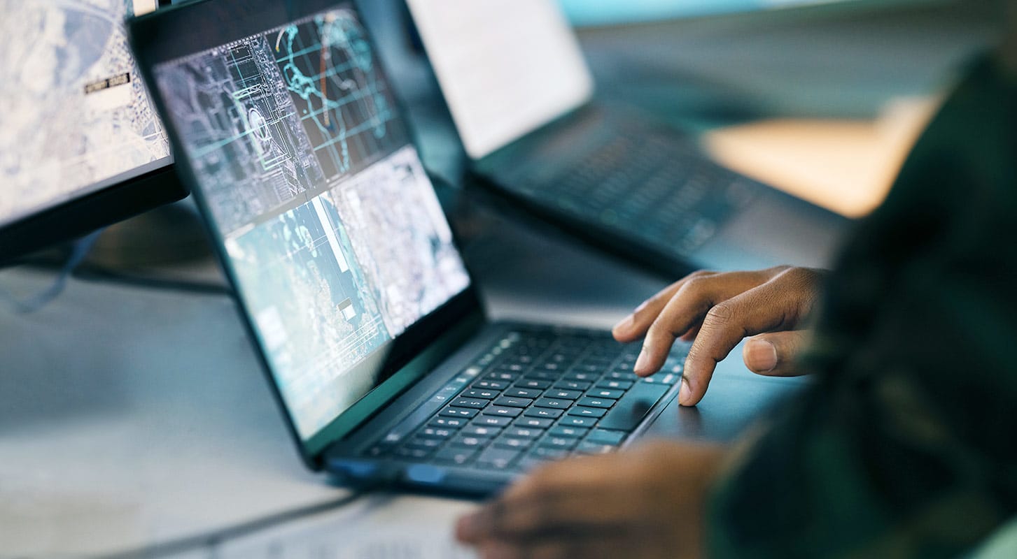 Individual using a laptop with a screen showing multiple geographical information data.